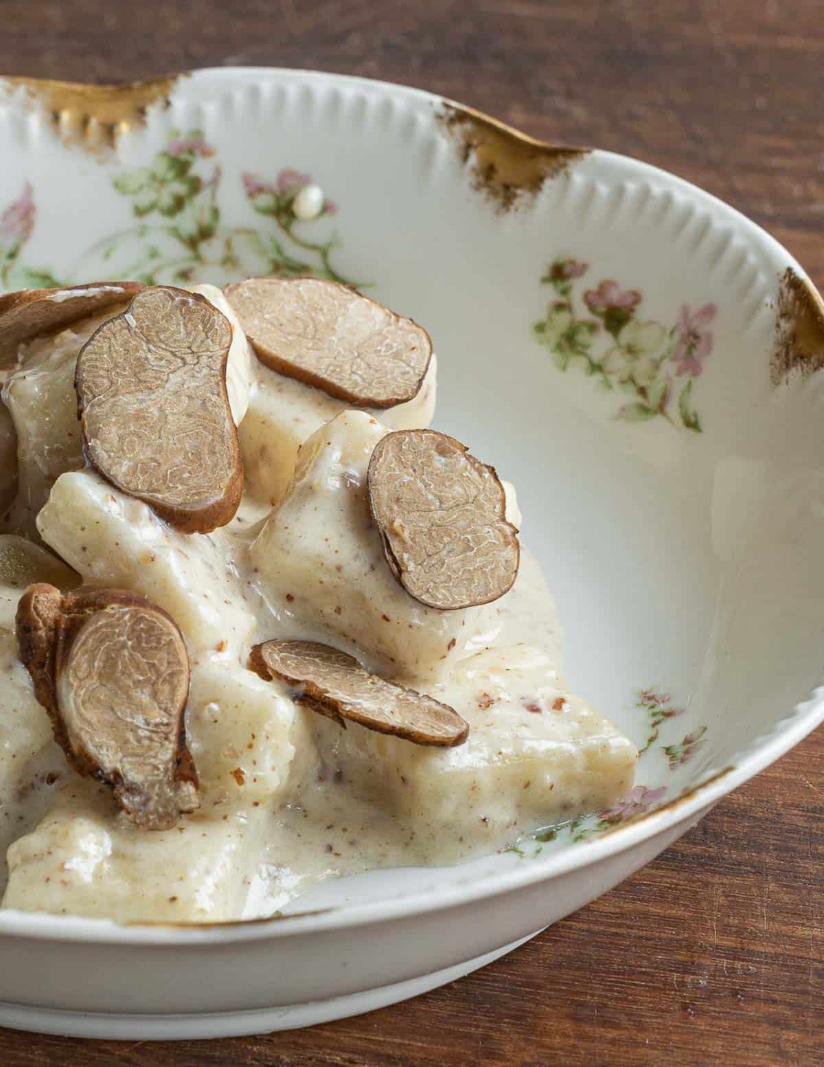 A china plate with gnocchi tossed in a pecan pesto cream sauce garnished with fresh sliced pecan truffles.