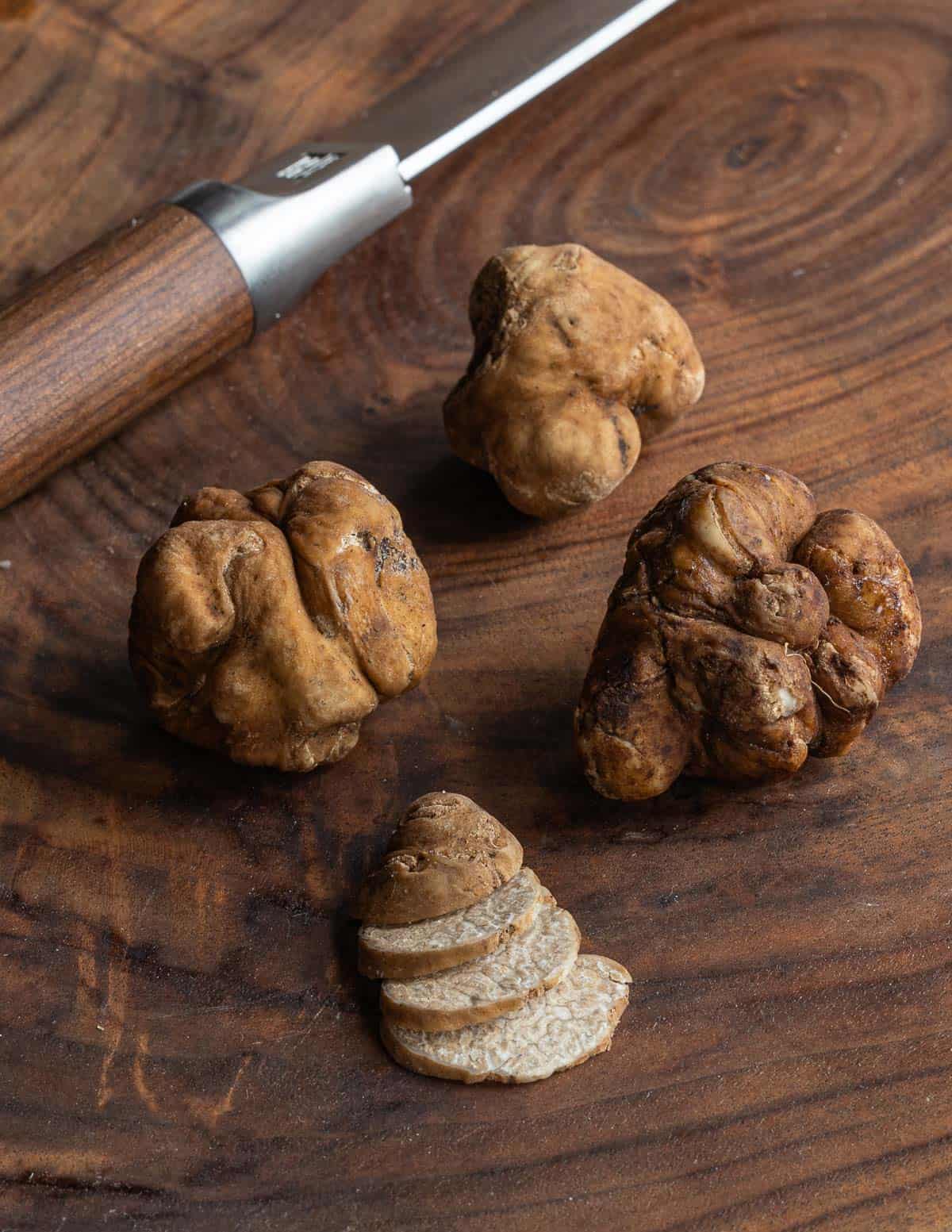 Sliced pecan truffles next to whole truffles and a paring knife. 
