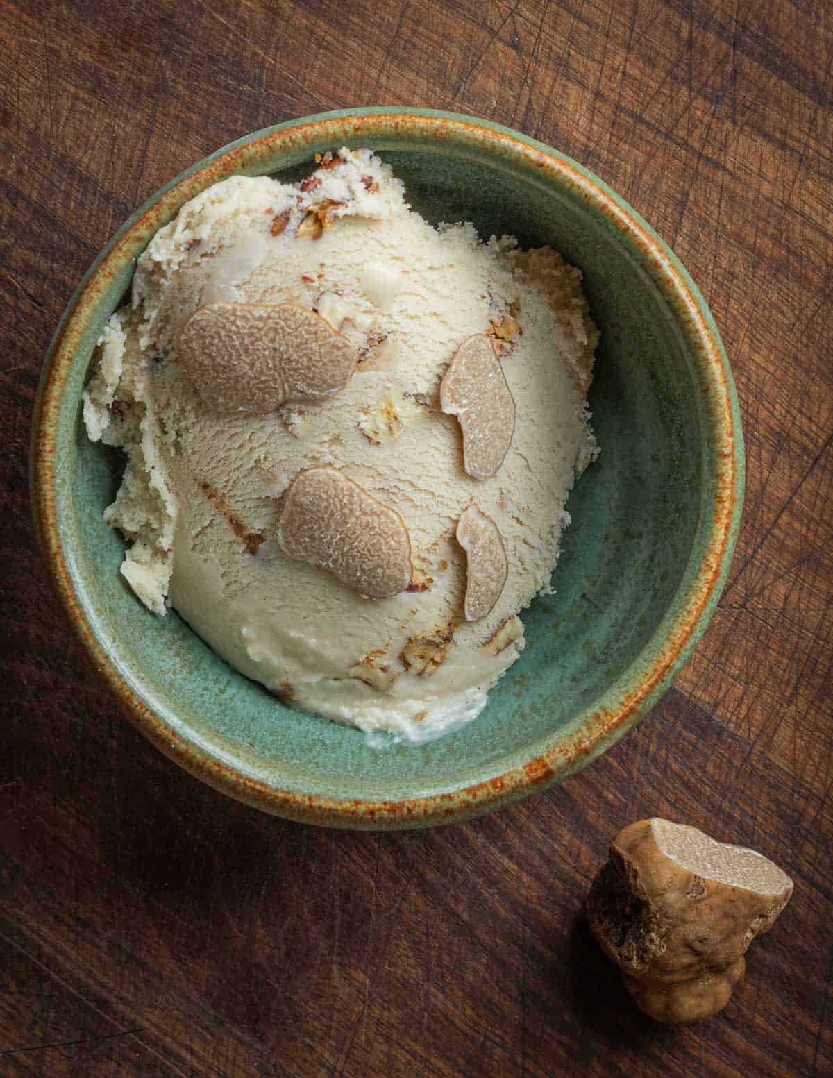 A green ceramic bowl with a scoop of truffle ice cream garnished with fresh sliced truffle mushrooms.