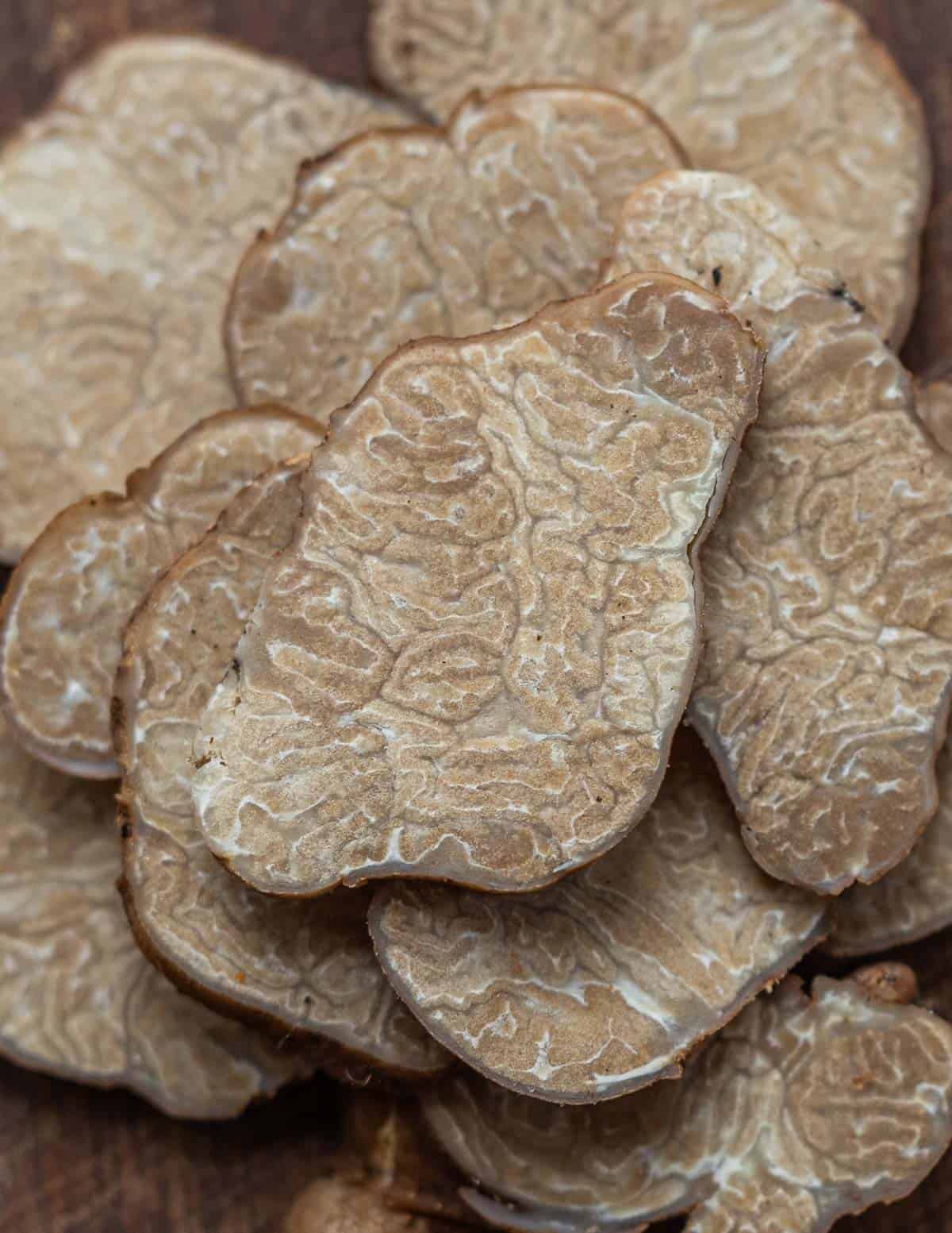 A close up image of a pile of freshly sliced pecan truffle mushrooms showing the marbled interior. 