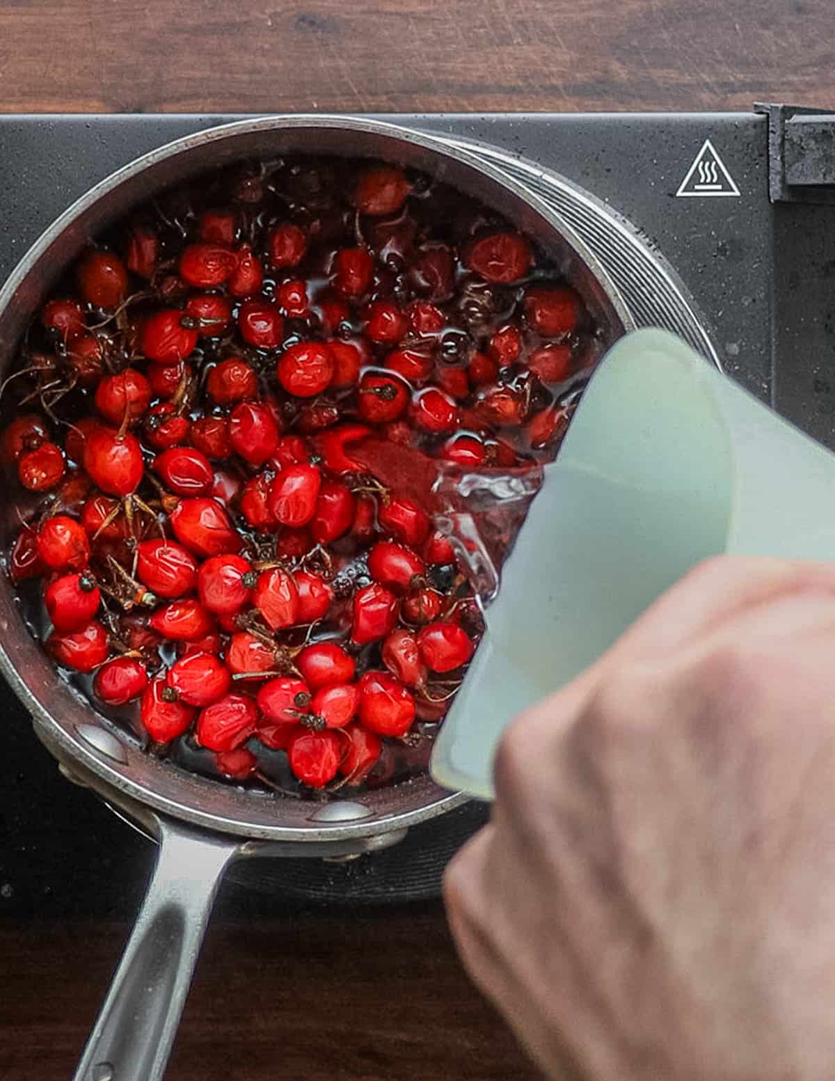 Pouring water over a pot of fresh wild rose hips. 