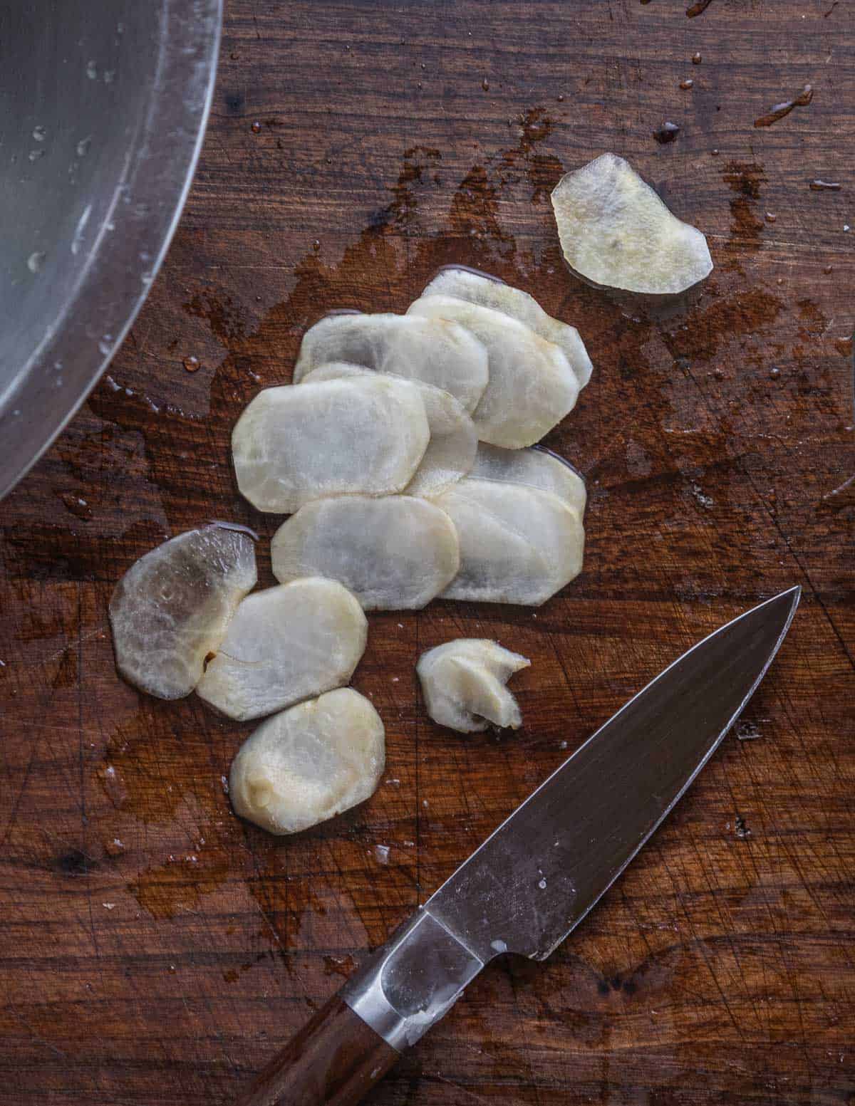 Thinly sliced sunchokes on a cutting board. 