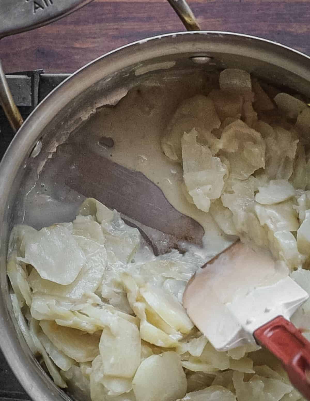 Stirring a pot of cooking sunchokes with a spatula showing the bottom of the pot. 