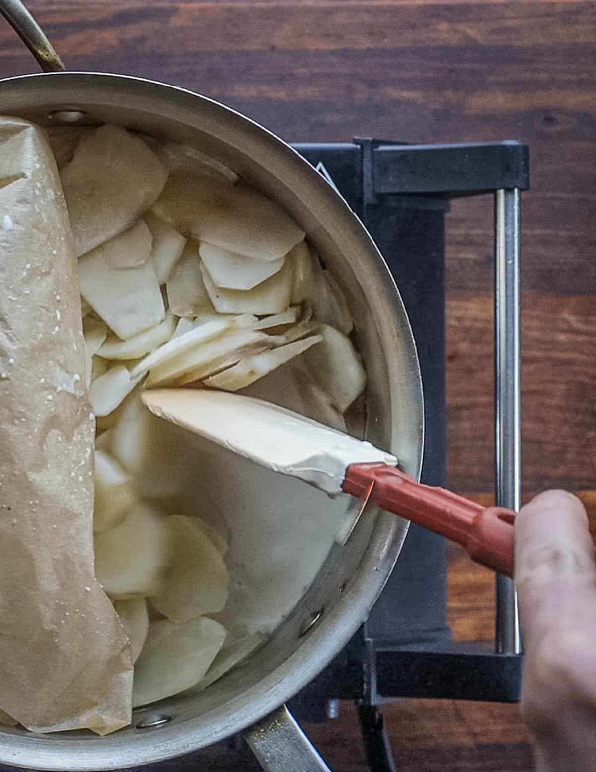 Pulling back parchment paper to stir a pot of cooking sunchokes. 