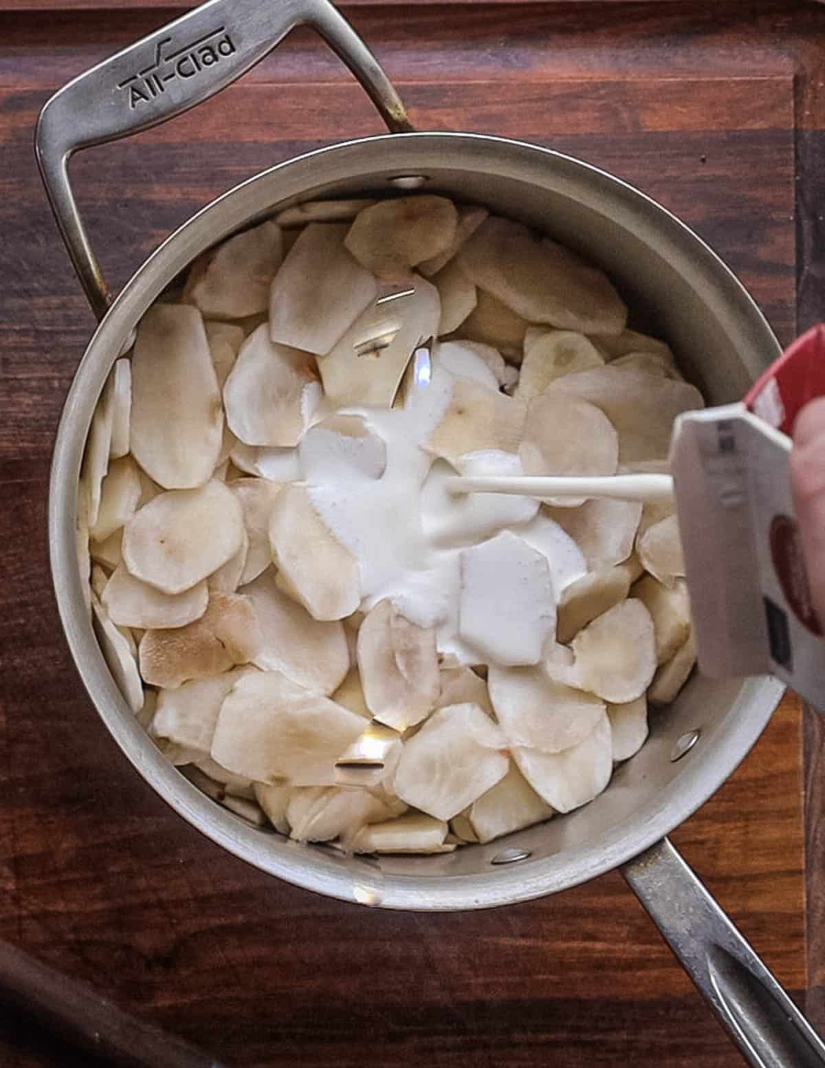 Pouring heavy cream into a pot of thinly sliced sunchokes. 