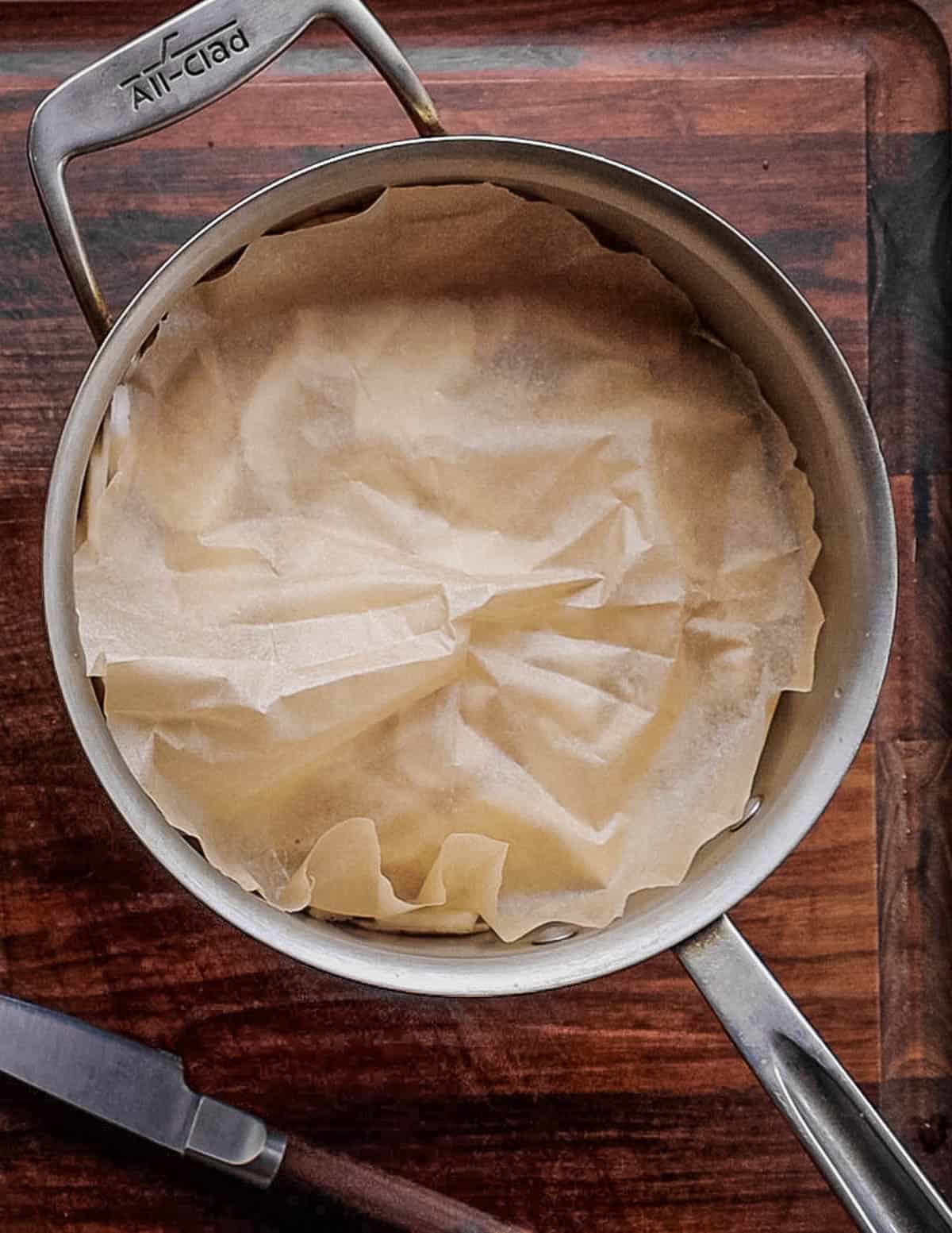 Putting a parchment lid on top of a pot of sunchokes. 