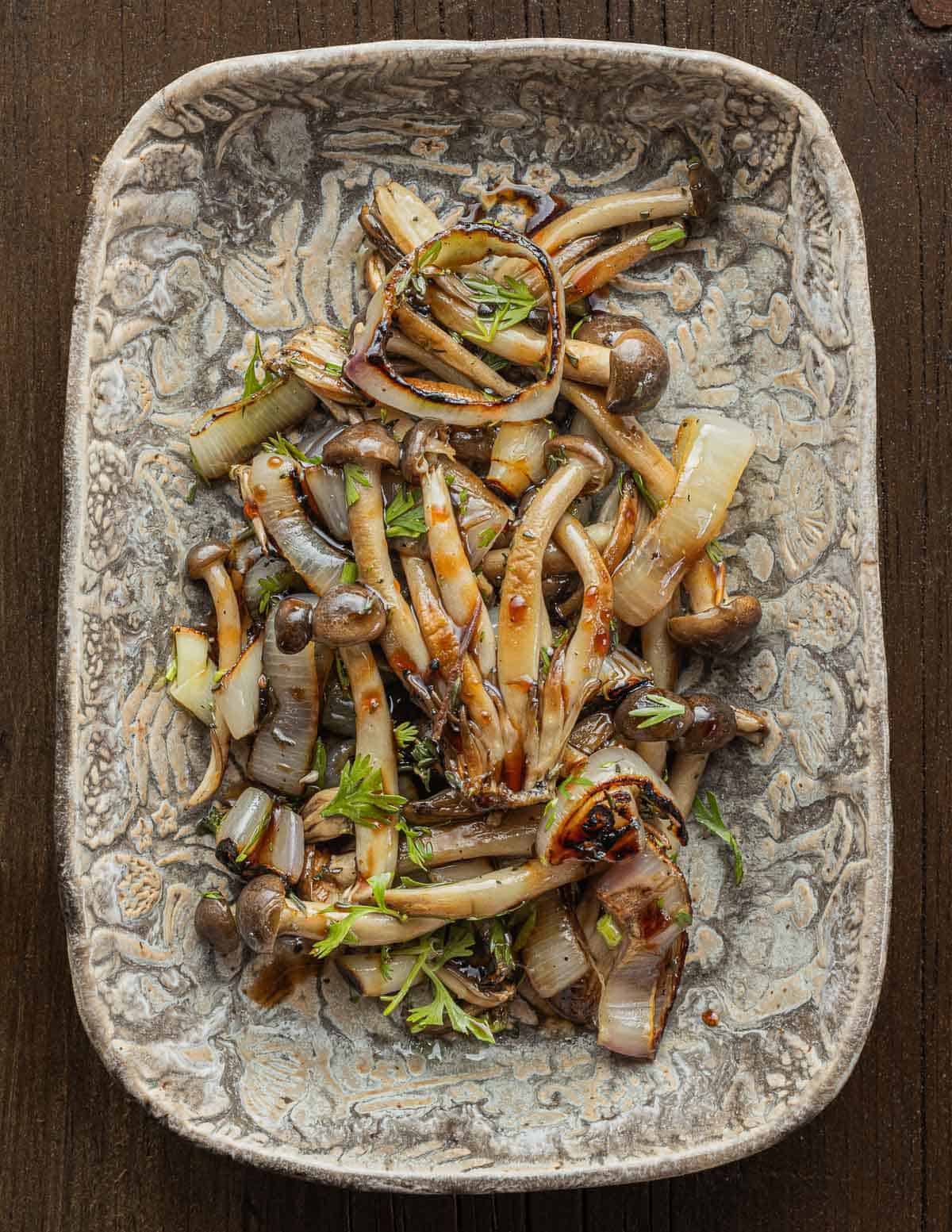 Marinated beech mushrooms mixed with shallots and balsamic vinegar in a ceramic serving dish. 