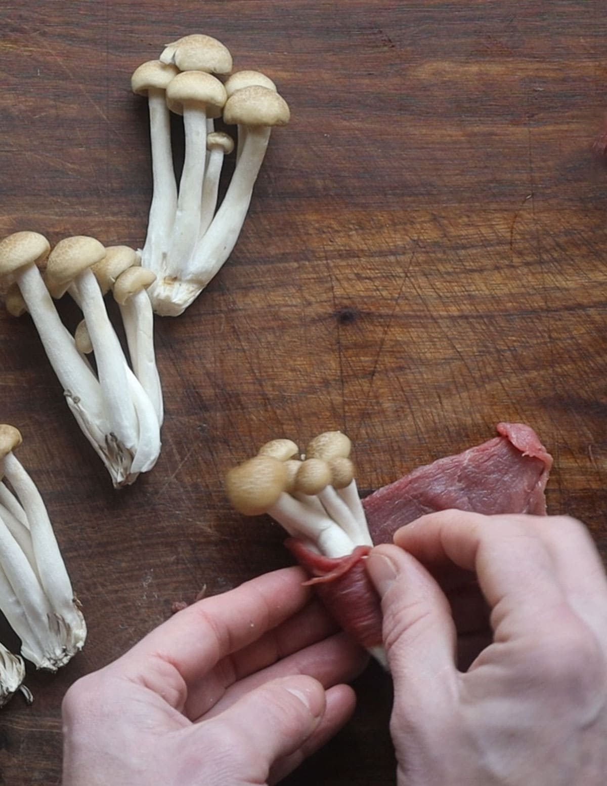 Wrapping clusters of brown beech mushrooms in thinly sliced meat. 