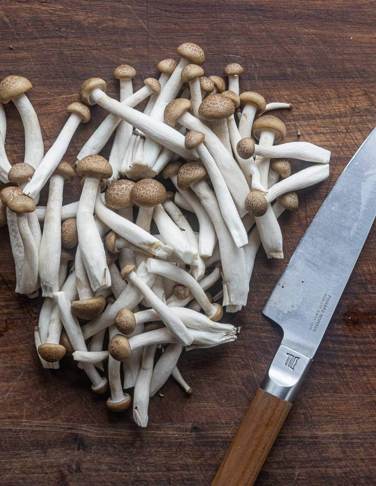 Shimeji mushrooms separated into pieces on a cutting board next to a knife. 