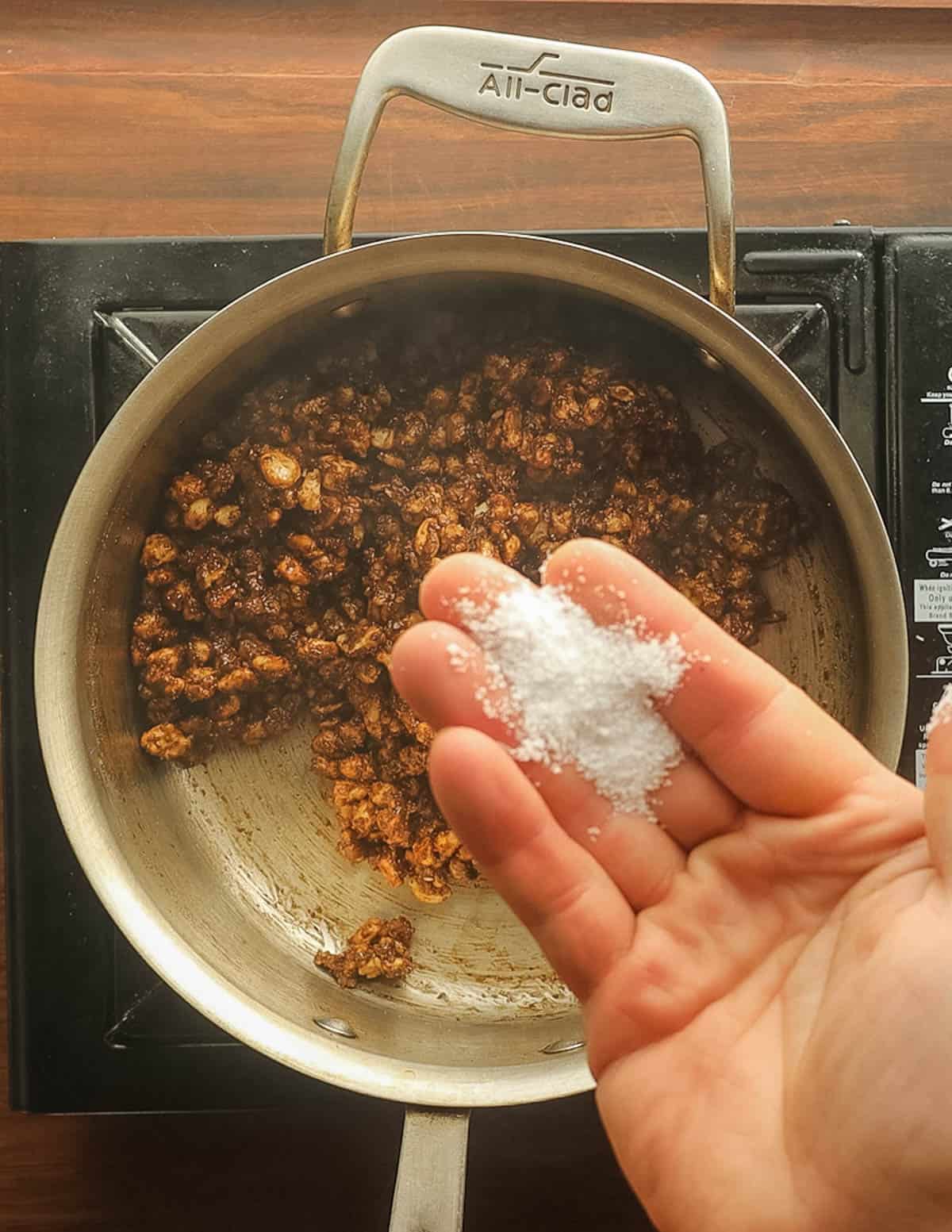 An open palm with salt about to be added to a pan of candied black walnuts. 
