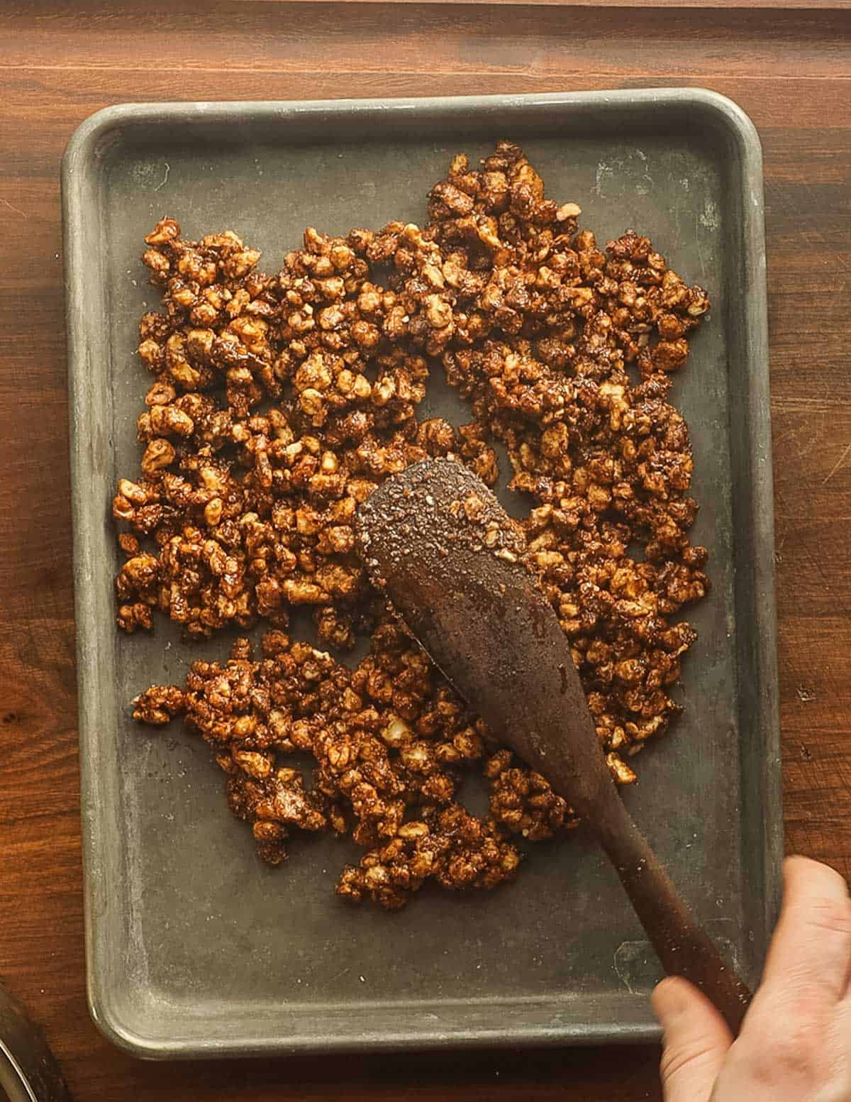 Spreading candied black walnuts on a baking sheet witha spatula. 