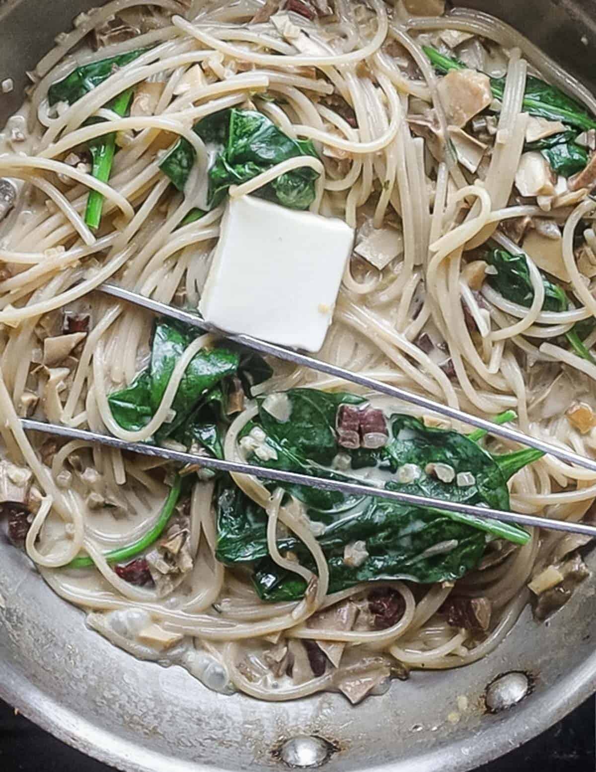 Adding butter to a pan of noodles with creamy mushroom sauce. 