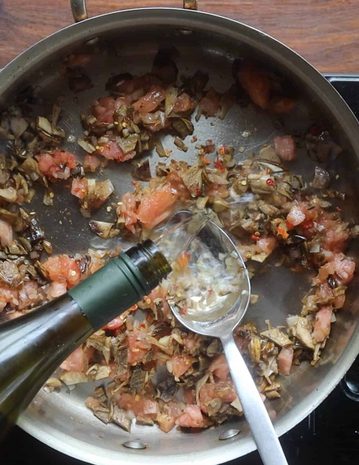 Adding white wine to a pan of cooking mushrooms, tomatoes and shallots. 