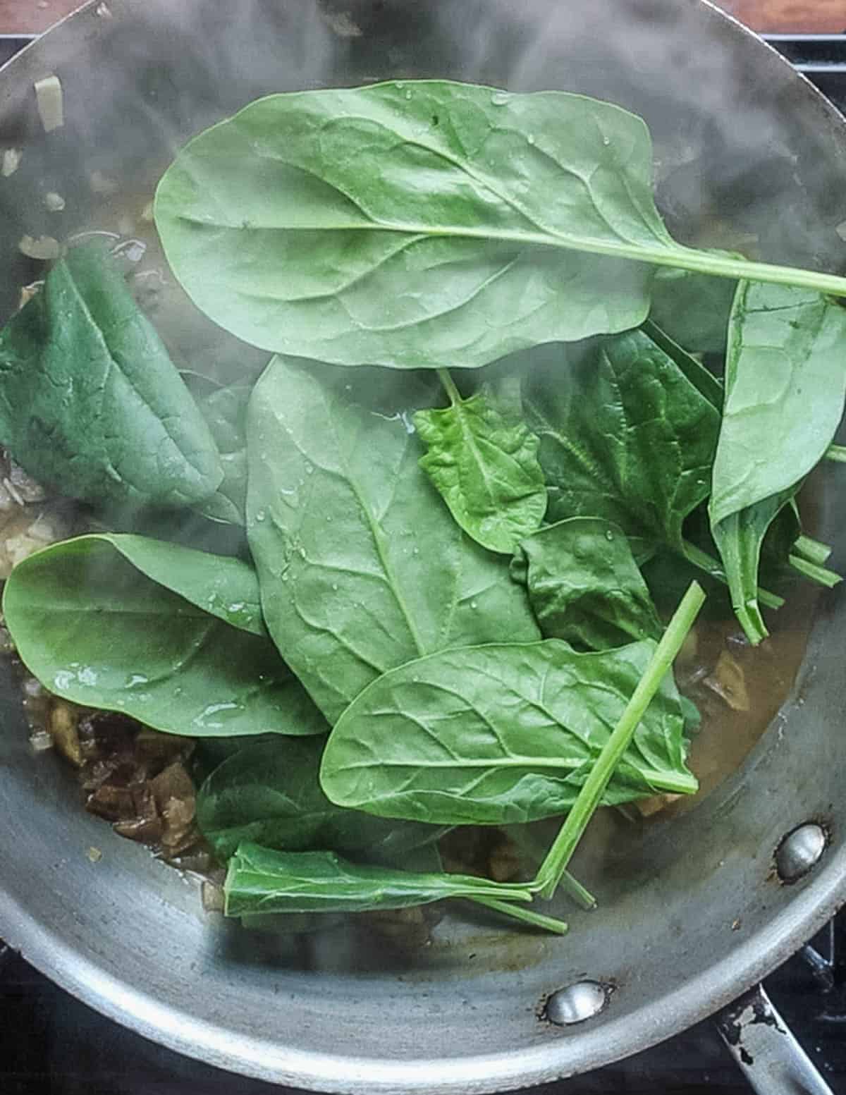Adding trimmed fresh spinach leaves to a pan of pasta to wilt it. 