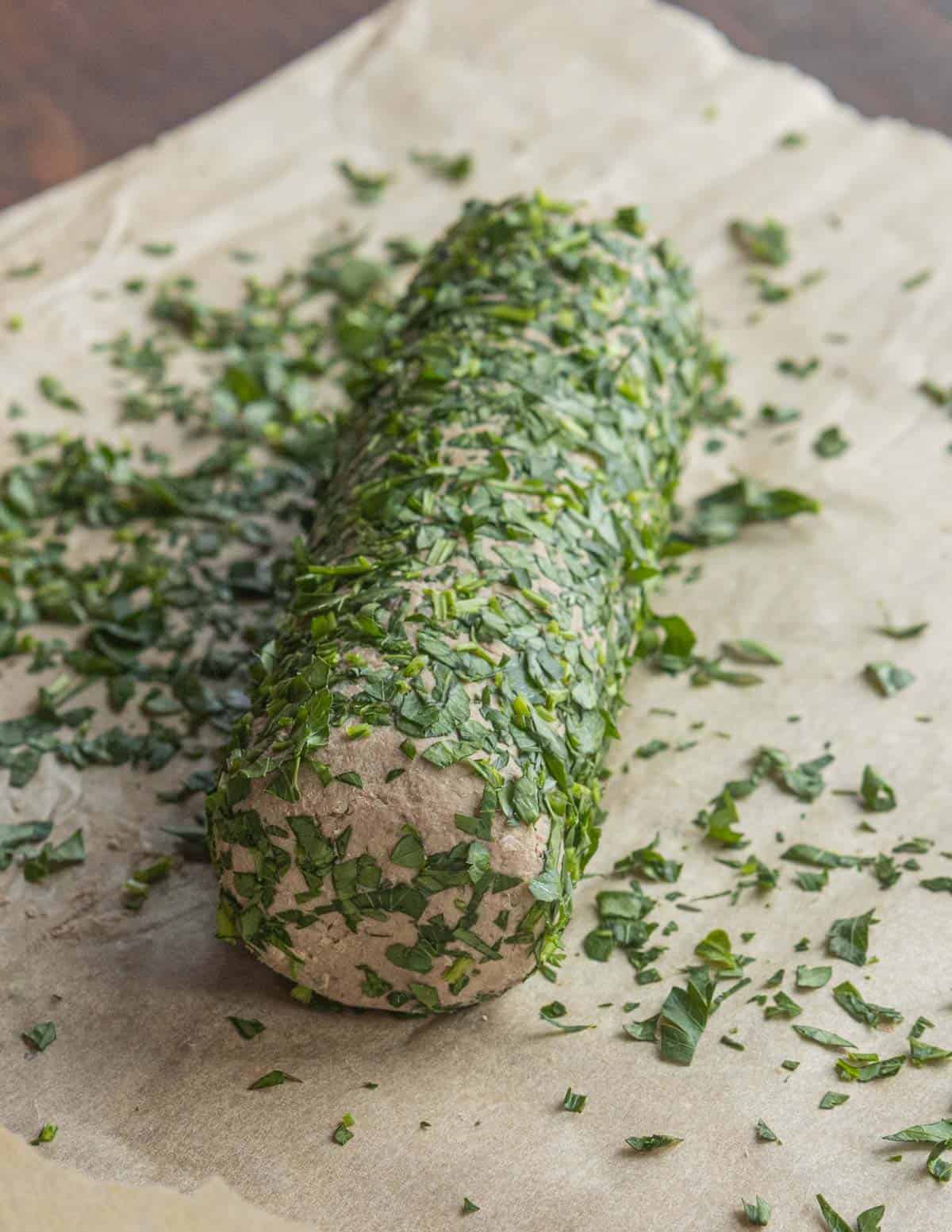Rillettes molded into a log being rolled in chopped fresh herbs. 