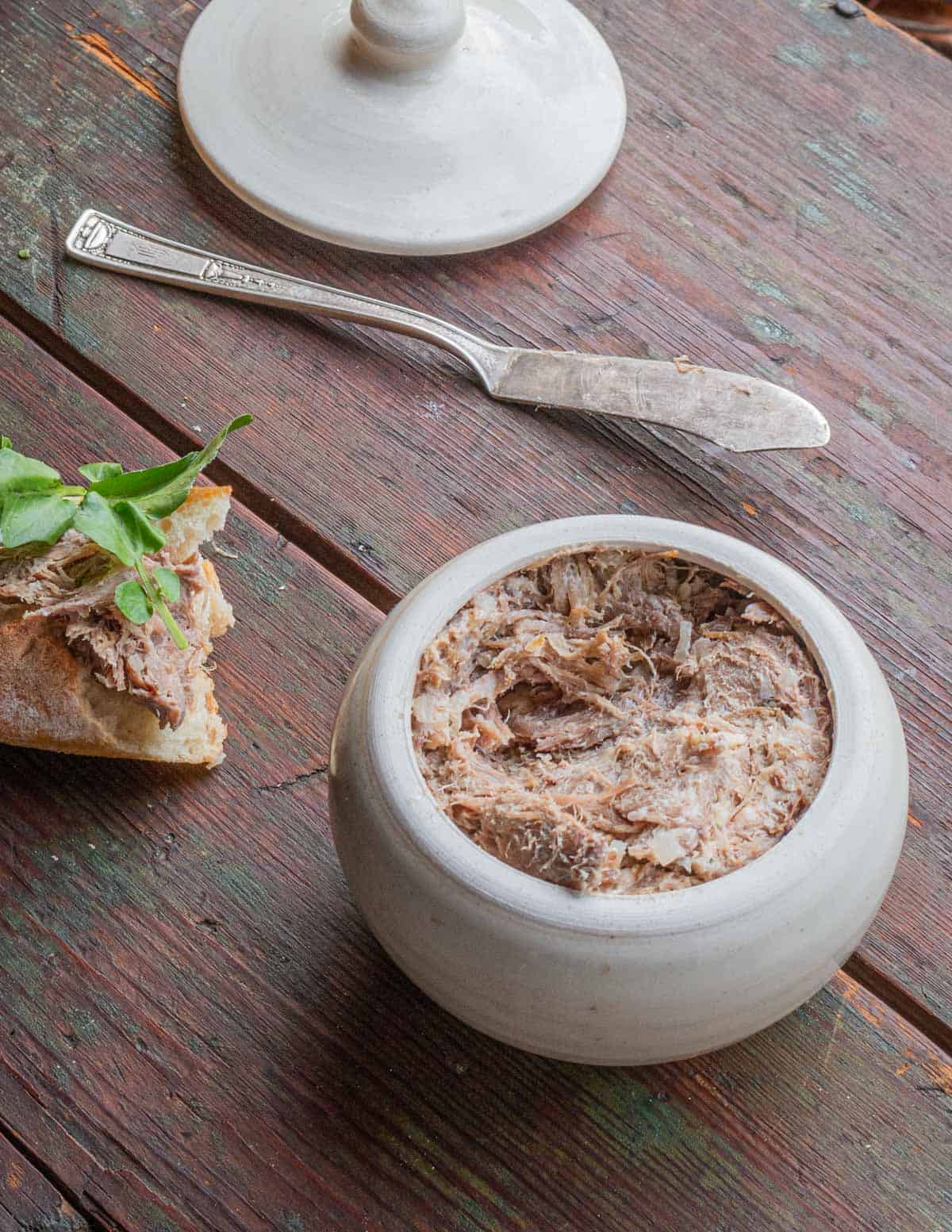A crockful of rillettes being served on a baguette with a piece of watercress. 