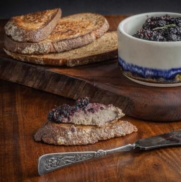 A toast point spread with rillettes and preserves next to a crock of preserves, sourdough bread and a spatula.