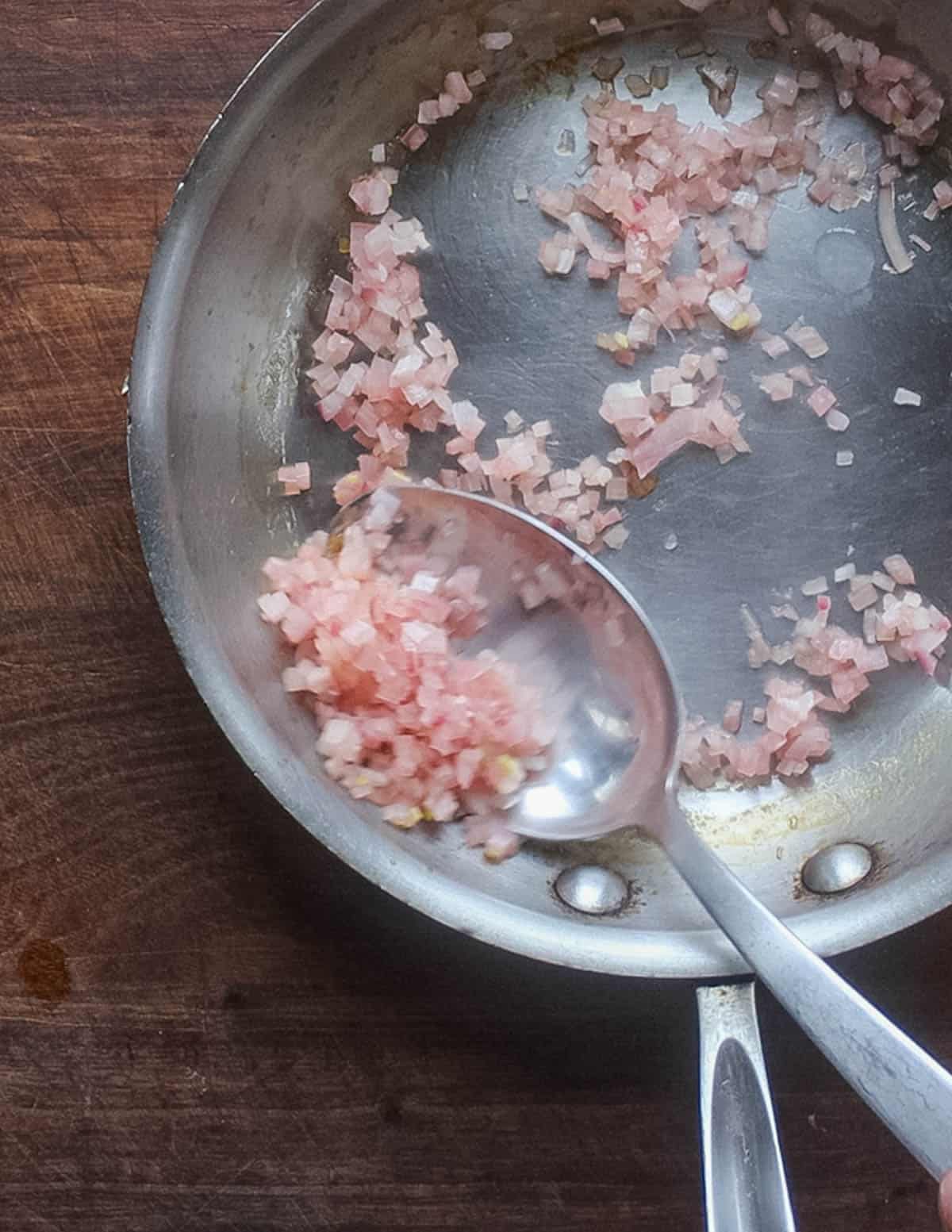 A spoon stirring a pan of diced shallots cooking in vinegar. 