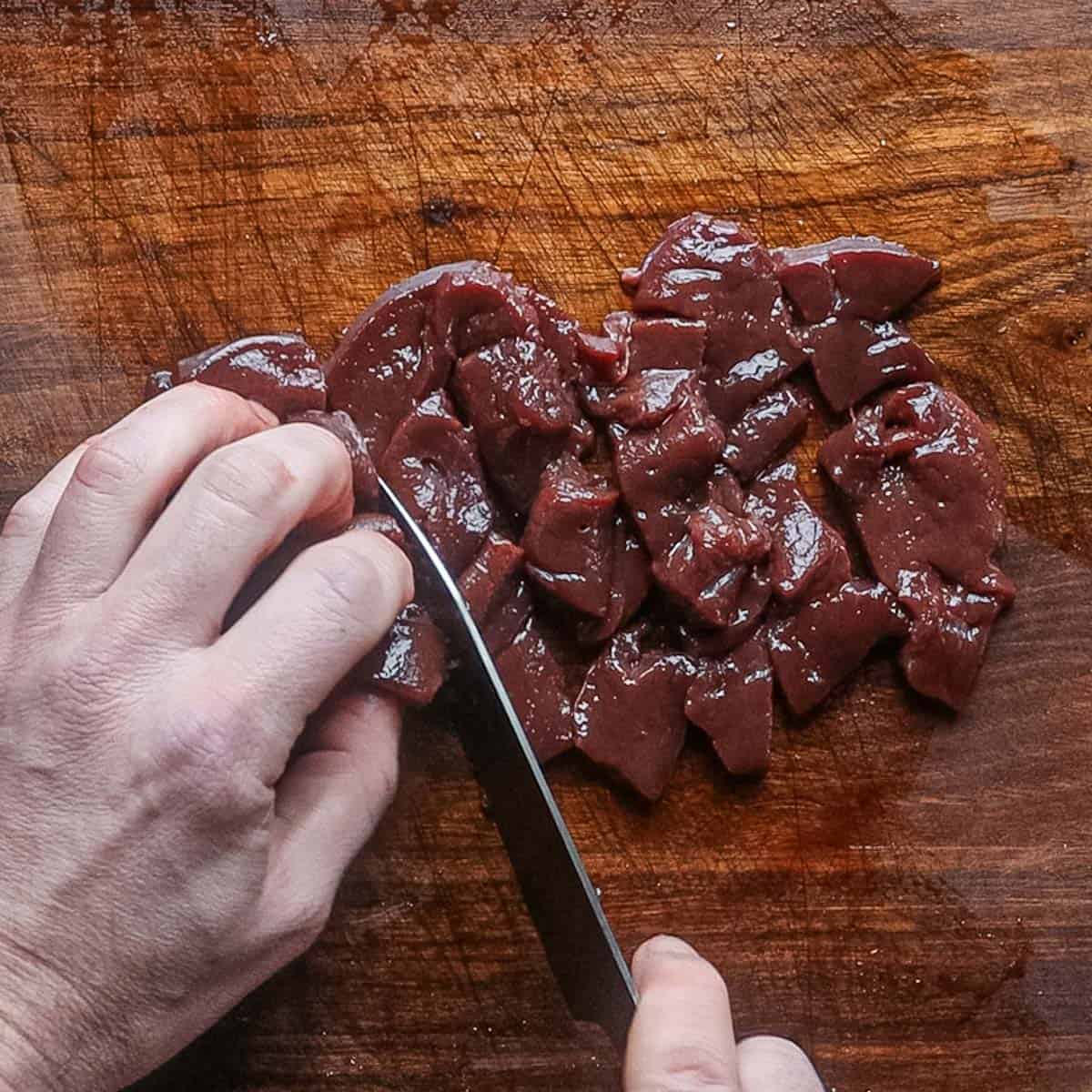 Slicing liver into cubes on a cutting board with a knife. 
