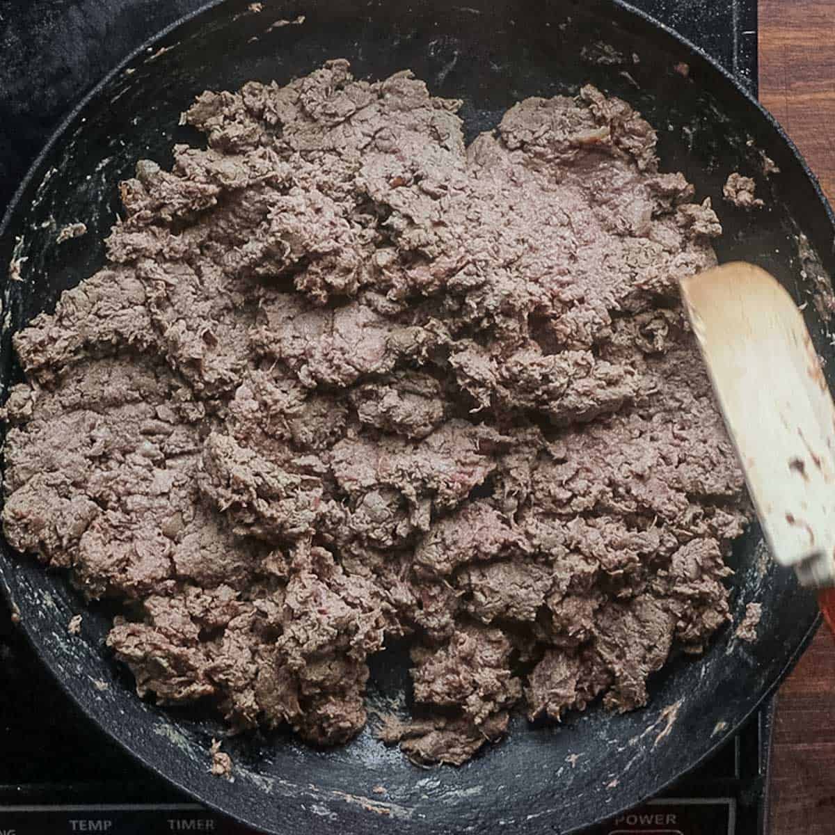 A pan of grey cooked liver being stirred with a rubber spatula. 