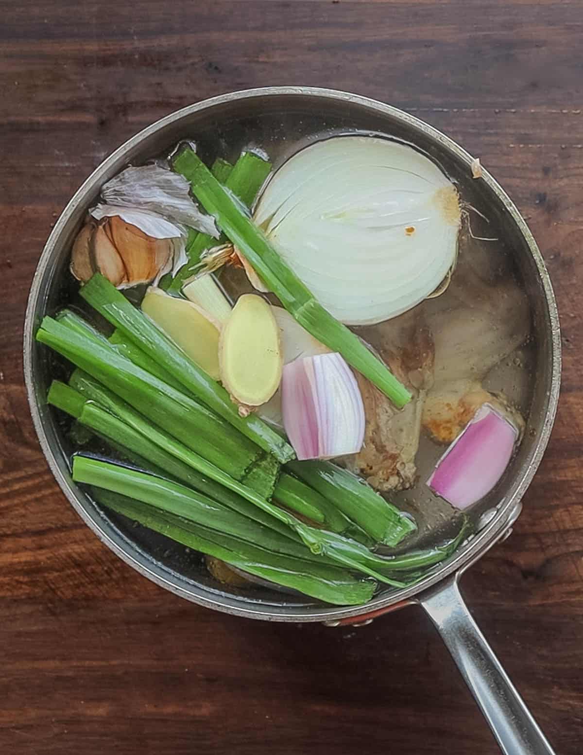 A pot of water with roasted chicken and asian ingredients ready to cook into broth.