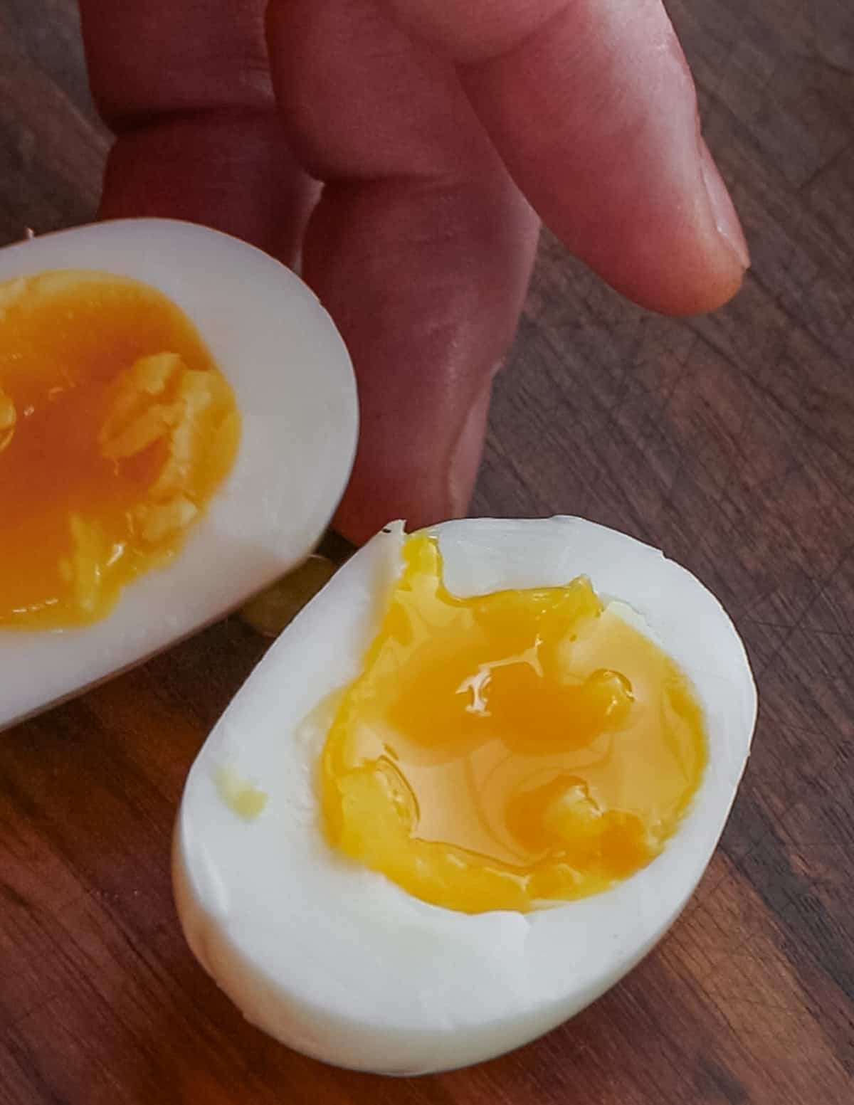A perfectly cooked six minute egg cut in half with yolk spilling out on a cutting board.  