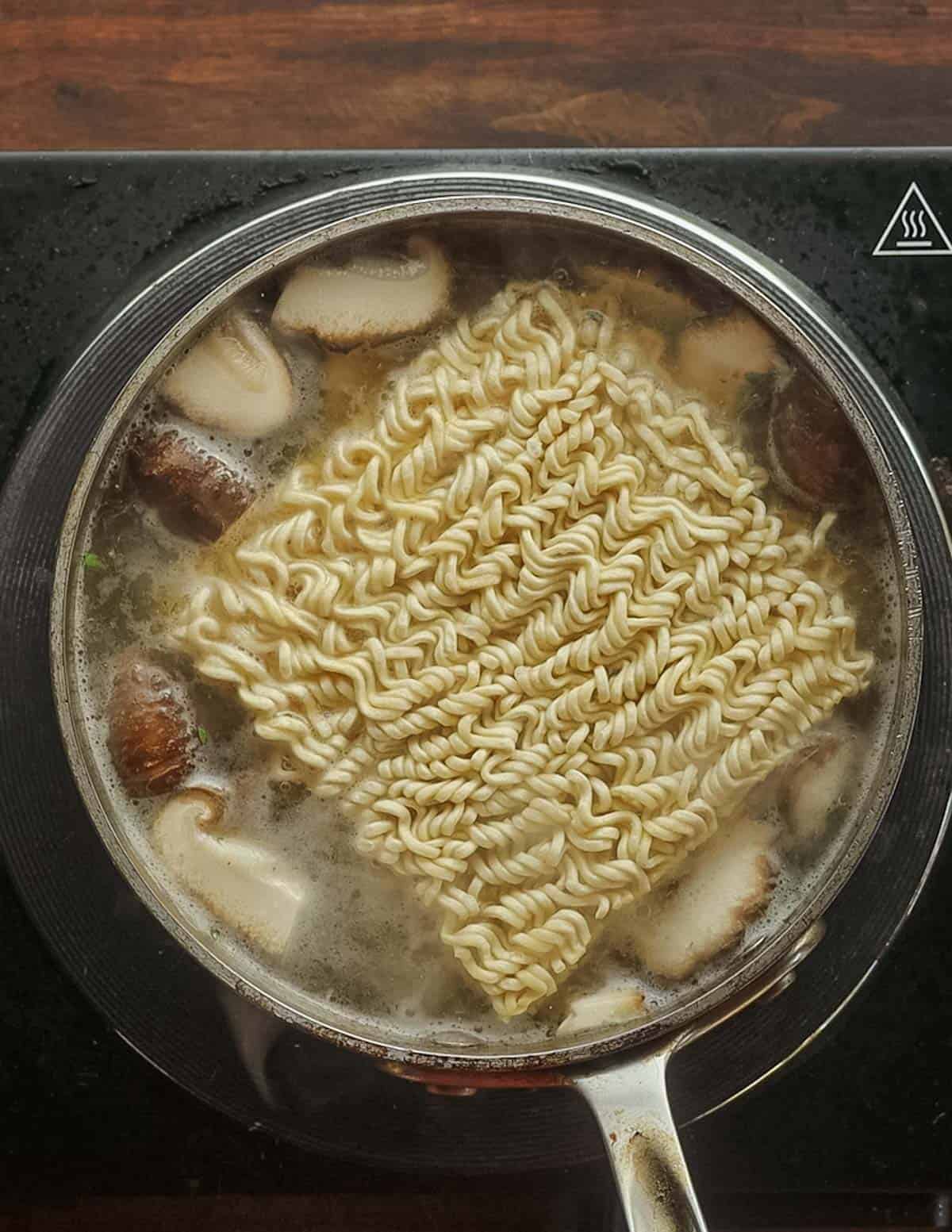 Adding dried ramen noodles to a pan of cooking broth. 
