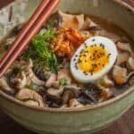 A bowl of wood ear mushroom ramen garnished with soft eggs, chicken skin and herbs served with chopsticks.