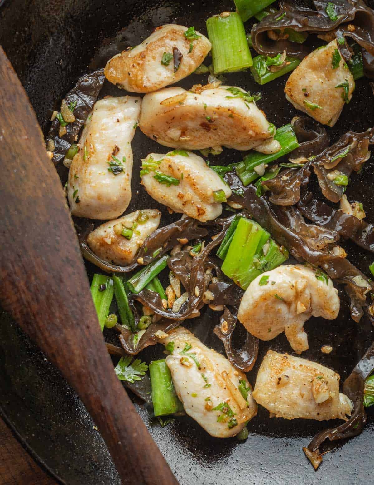 A pan of chicken and wood ear mushroom stir fry with a spatula. 