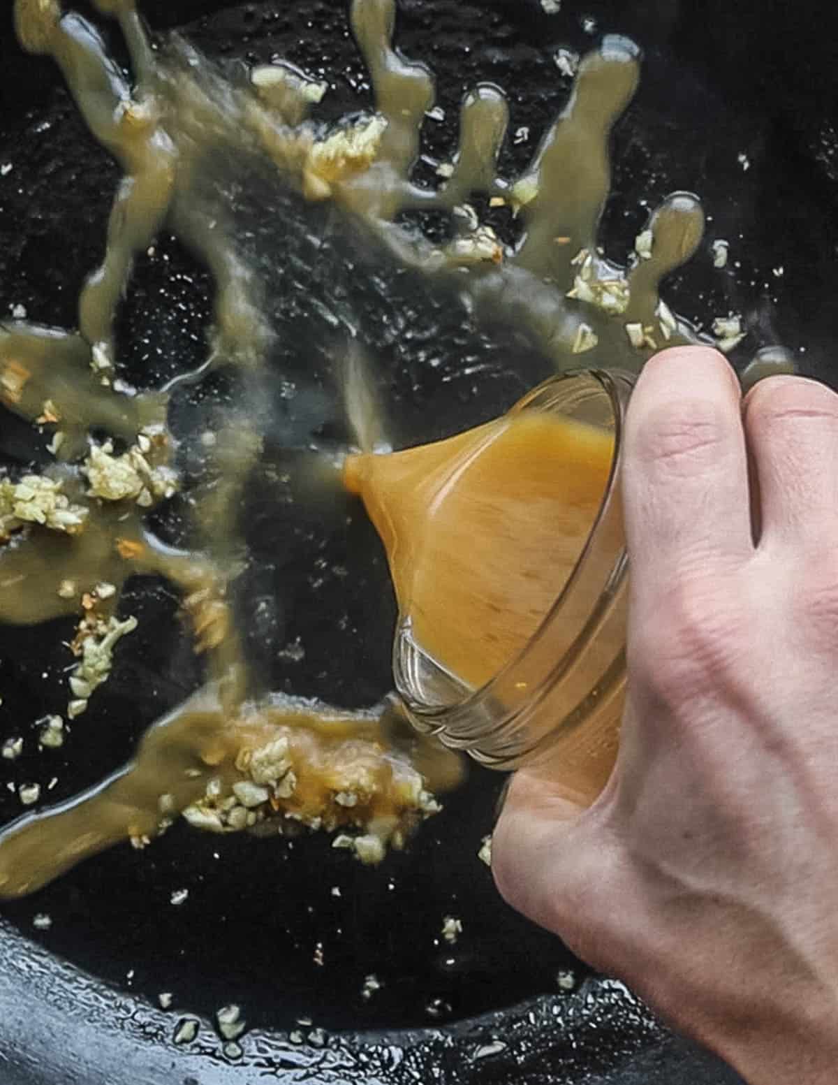 Pouring a hot and sour sauce into a pan of cooking garlic and ginger. 