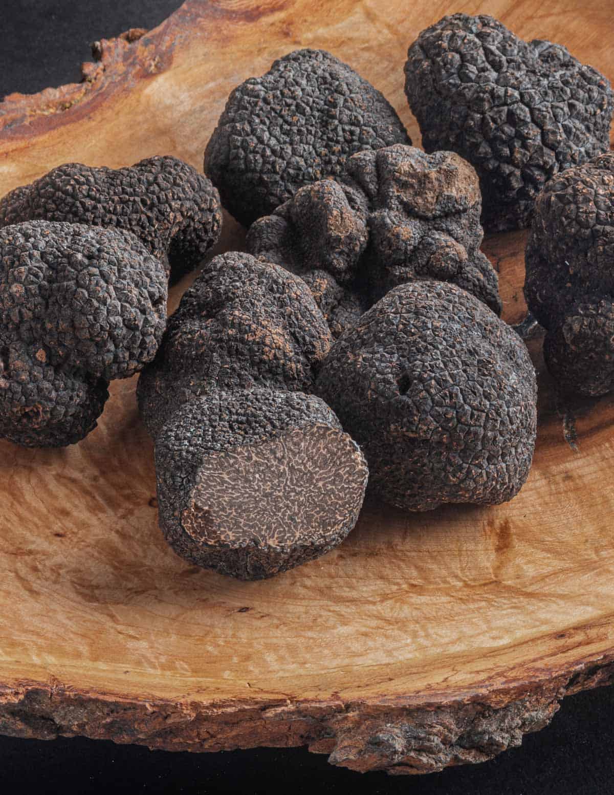 Many fresh black truffles (Tuber melanosporum) on a wooden board. 