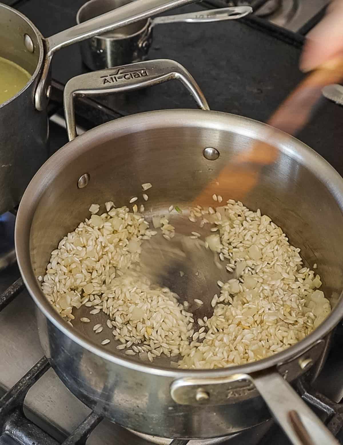 Adding rice to a pot of onion for making risotto. 