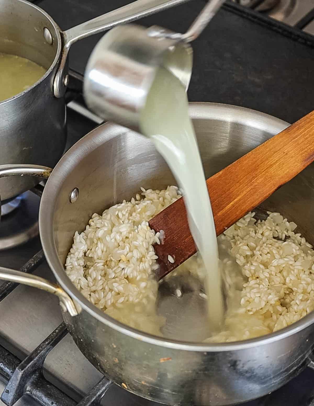 Adding chicken stock to a pot of risotto rice cooking. 