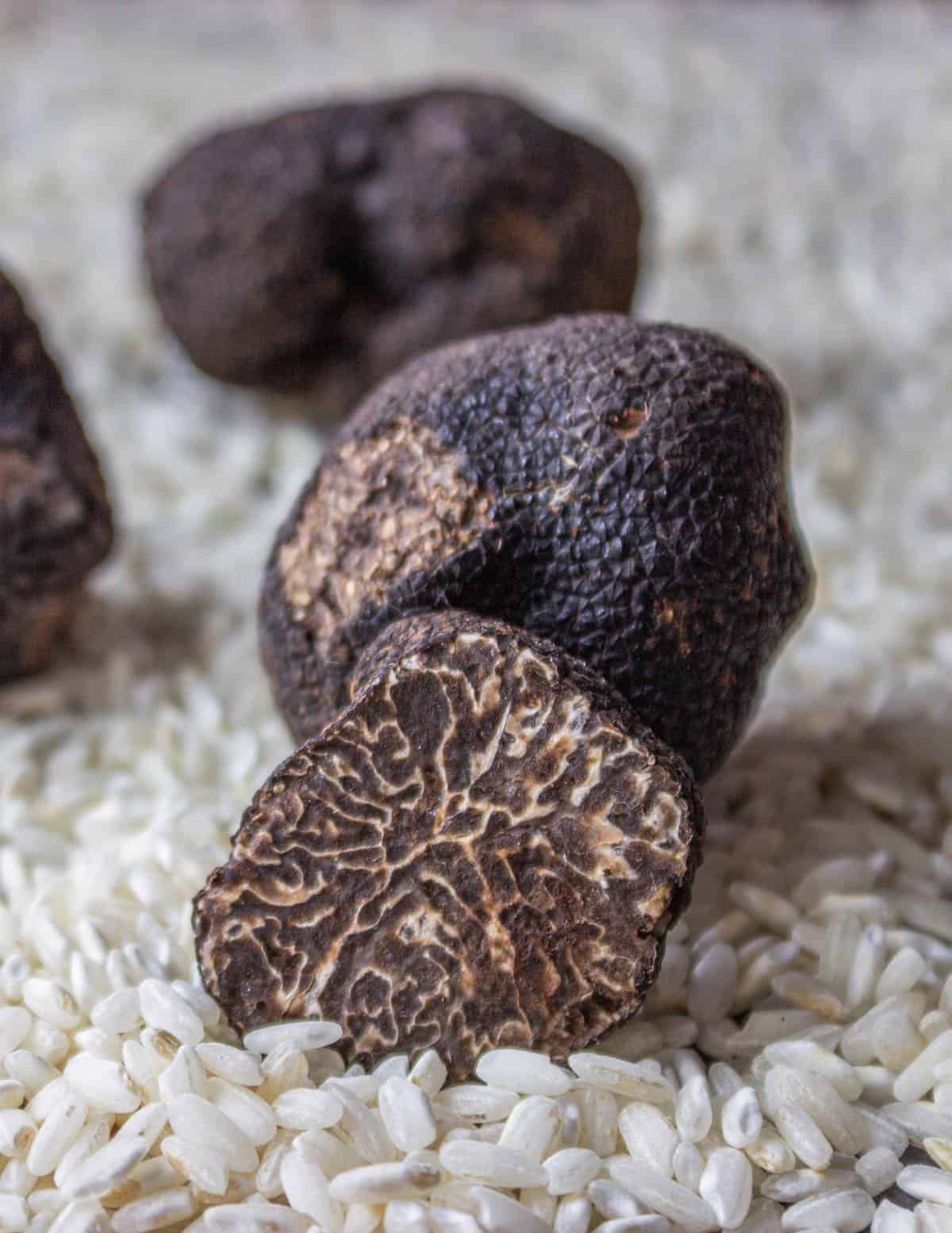 Tuber brumale black truffles cut in half to show the internal pattern, arranged on a pile of risotto rice before cooking. 