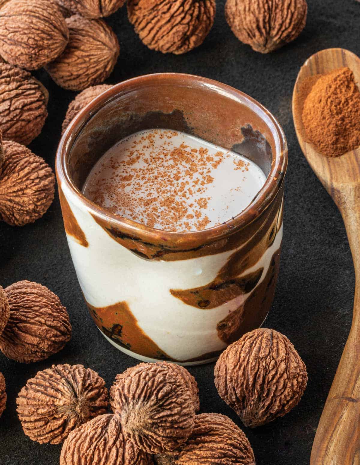 A glass of black walnut milk garnished with cinnamon next to whole black walnuts in the shell. 