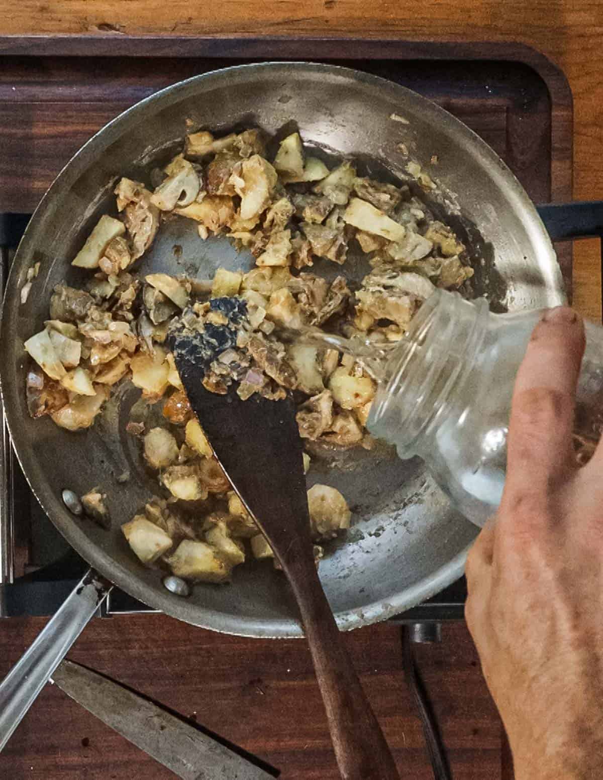 Adding a splash of water to a pan of cooking mushrooms. 