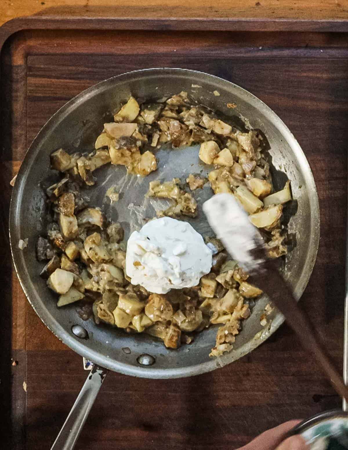 Adding sour cream to a pan of cooked mushrooms. 