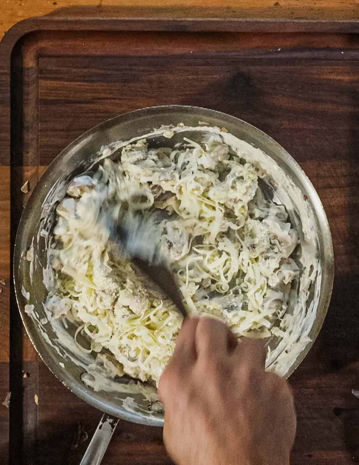 Adding parmesan and gruyere cheese to a pan of cooked mushrooms. 