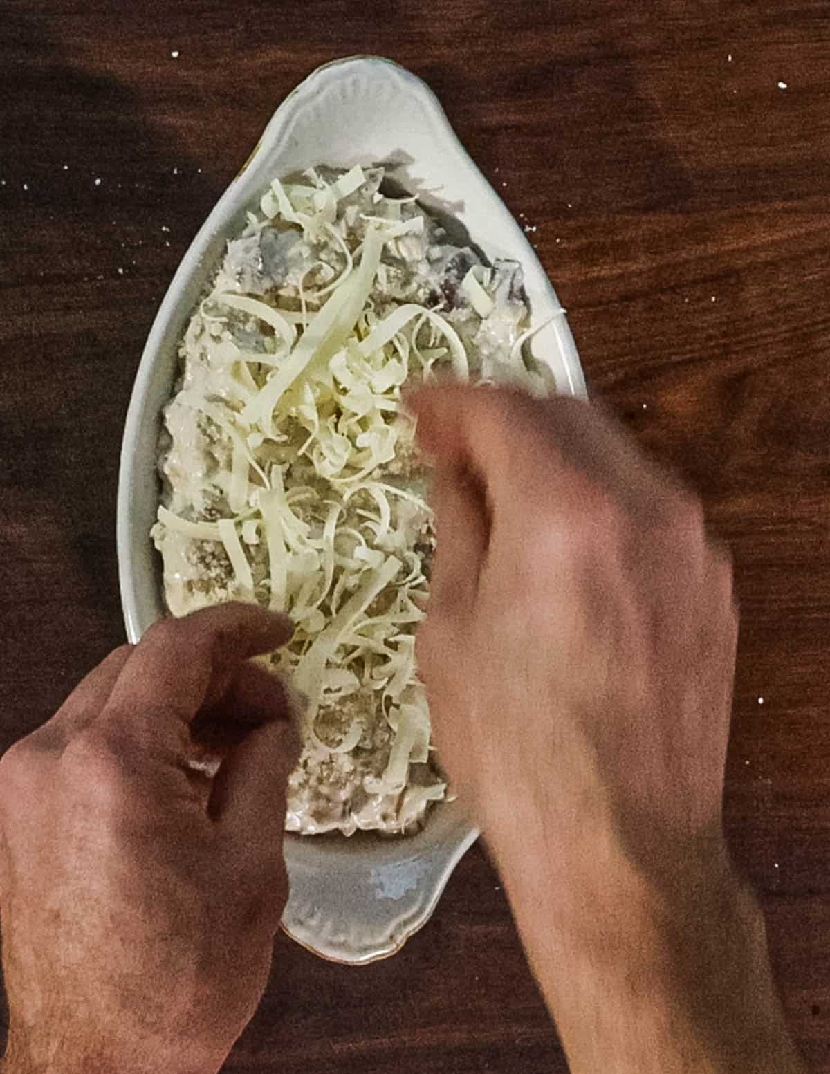 Putting cheese on top of a baking dish filled with mushrooms. 