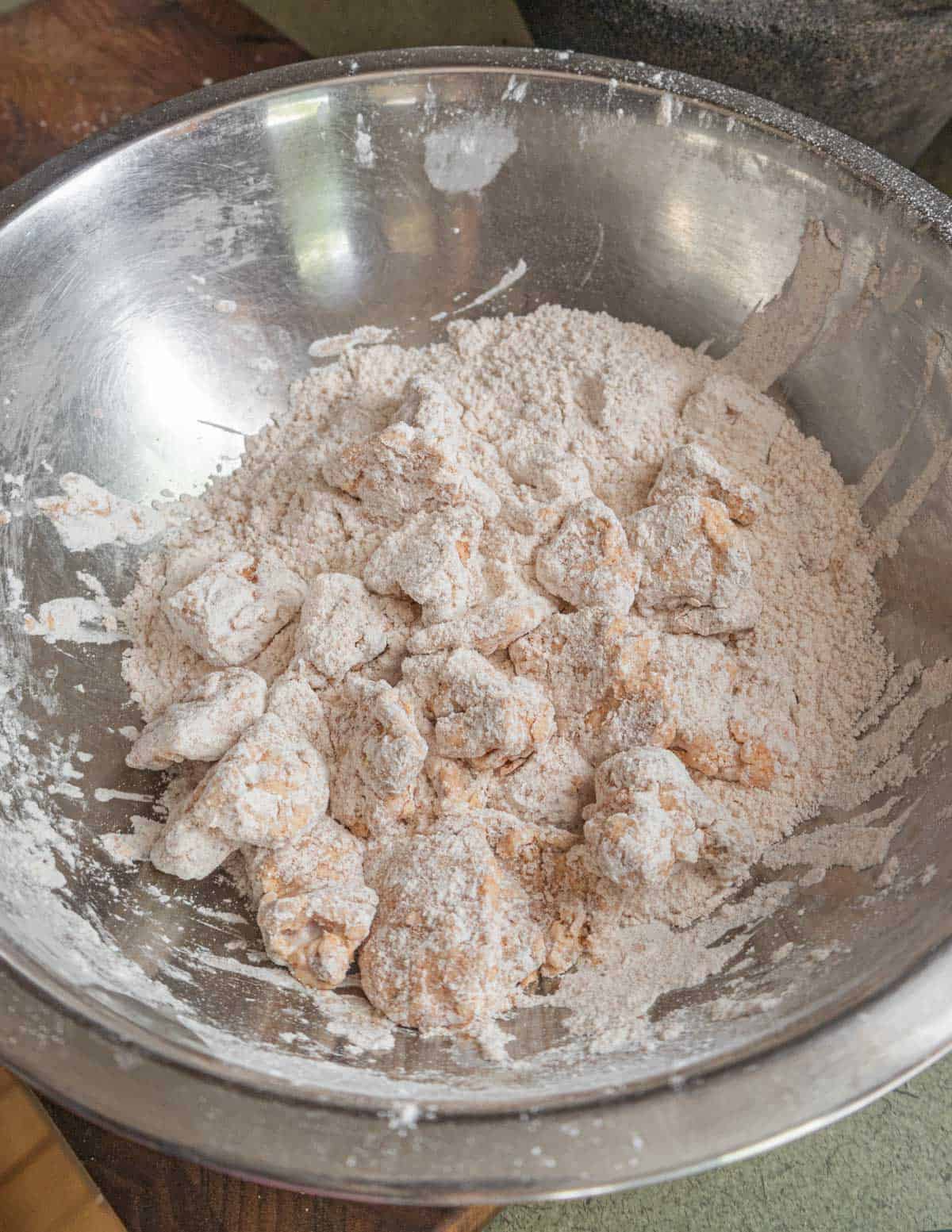 Mixing mushrooms in seasoned flour in a mixing bowl before frying.