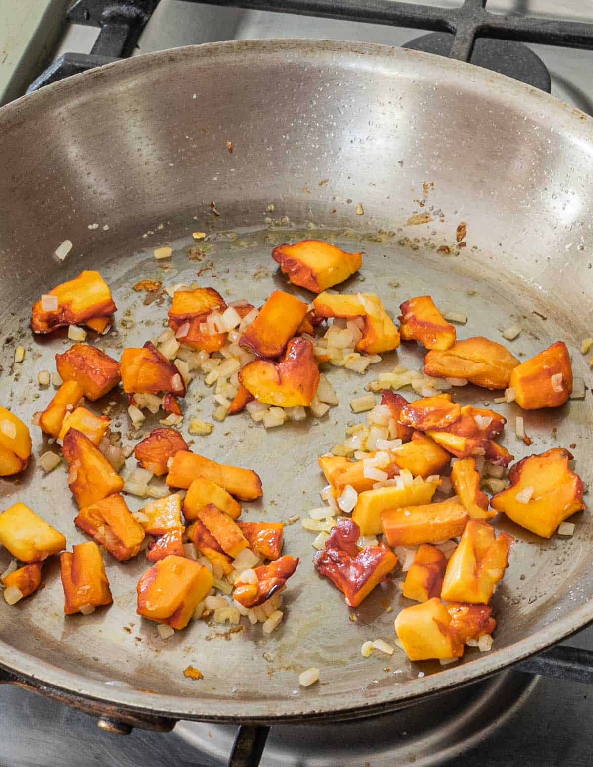 Adding chopped shallots to a pan of orange mushrooms. 