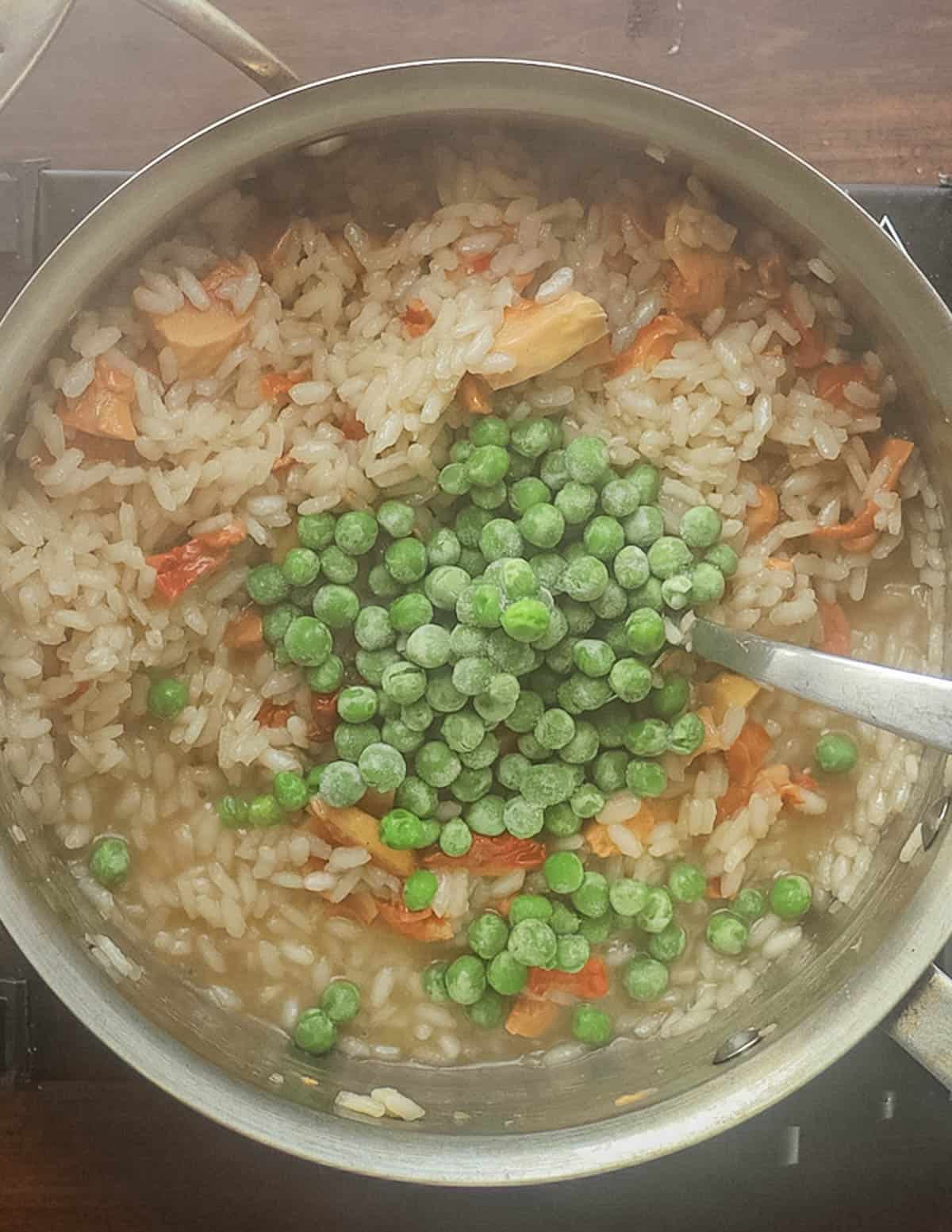 Adding frozen peas to a pot of risotto. 