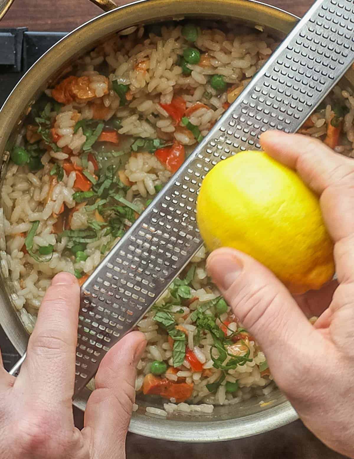Adding lemon zest and herbs to a pot of risotto. 