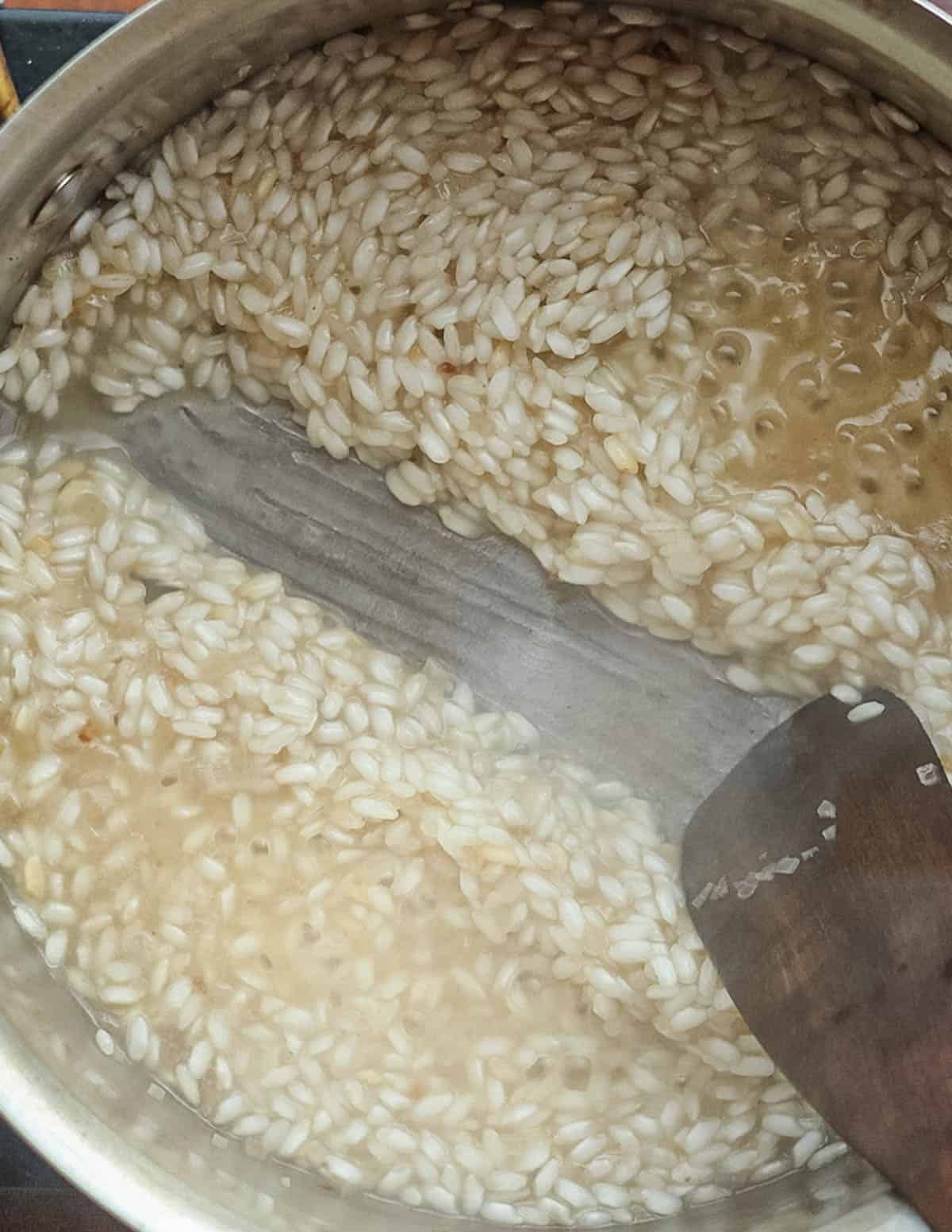 A spatula being dragged through a pan of cooking risotto rice.