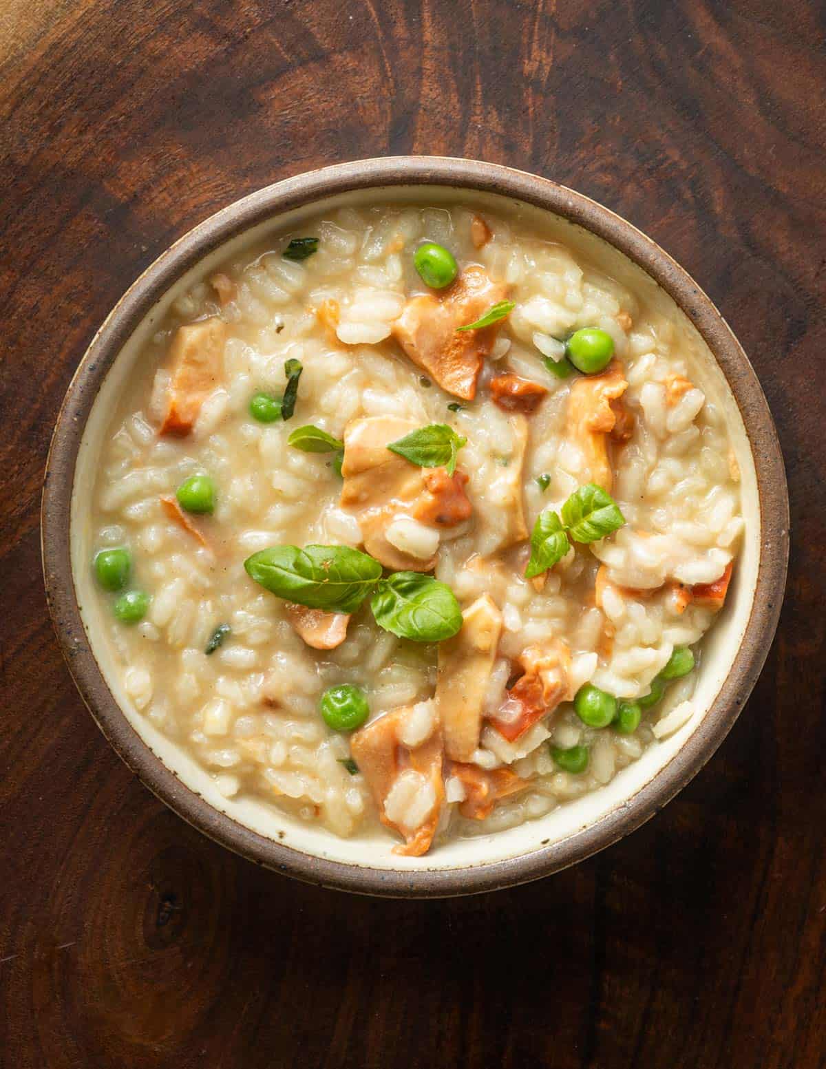 A bowl of wild chicken of the woods risotto with lemon and peas garnished with basil leaves. 