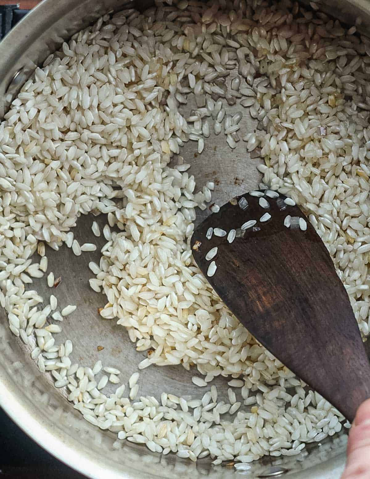 Adding risotto rice to a pot with cooking onion. 