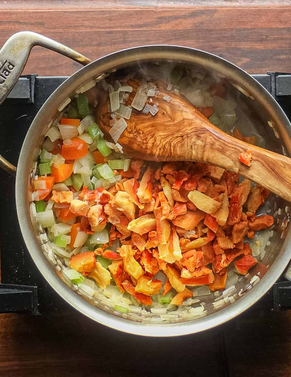 Adding chicken mushrooms to a pot of carrot onion and celery. 