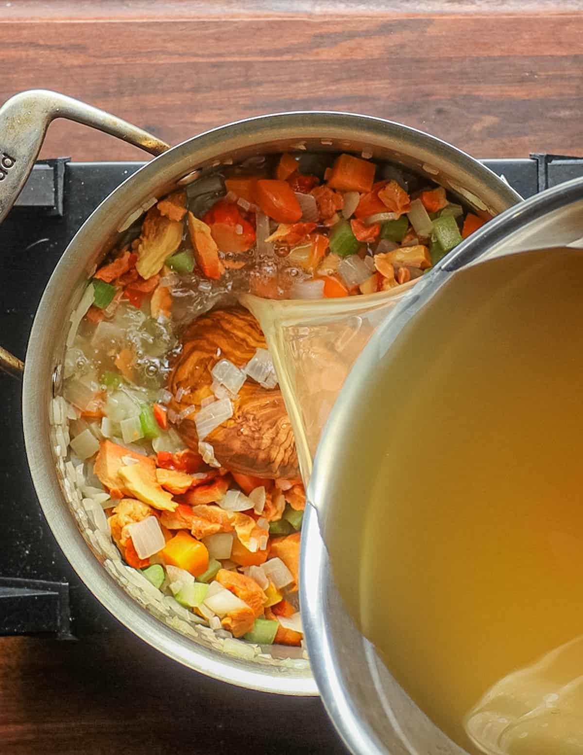 Adding chicken stock to a pan of chicken of the woods mushrooms and vegetables for soup. 