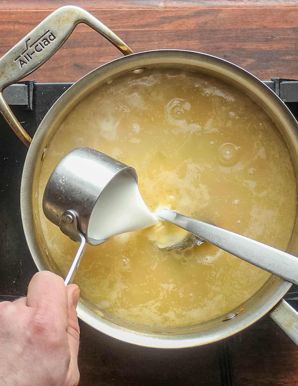 Adding cream to a pot of chicken mushroom soup. 