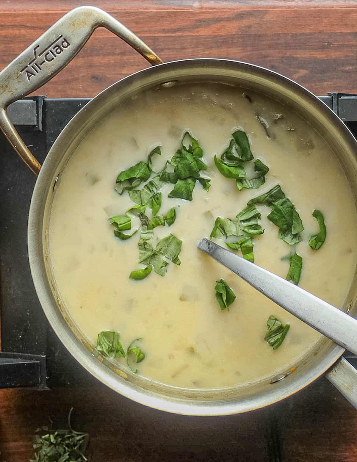 Adding fresh herbs like basil and tarragon to a pot of creamy soup. 